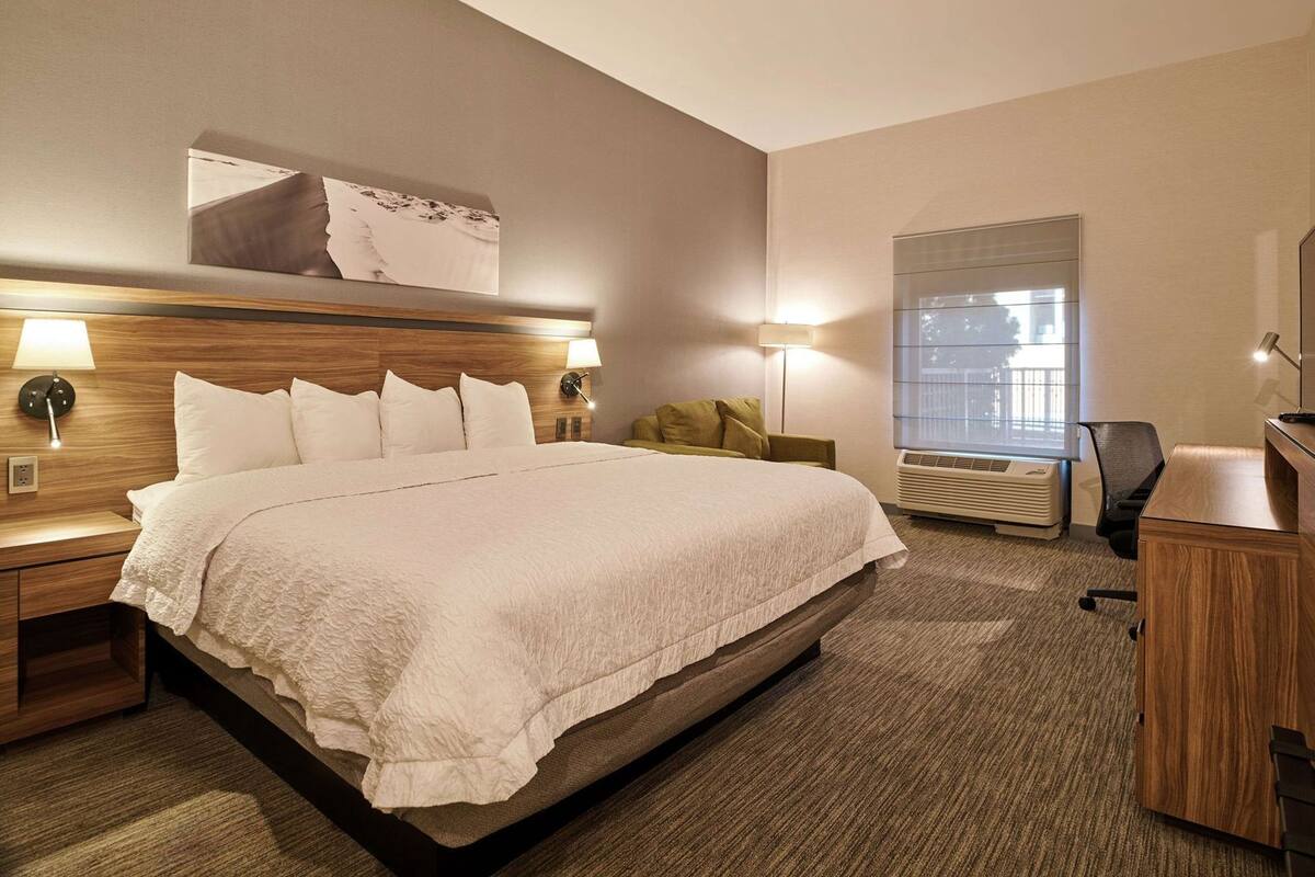 A hotel room with a large bed, bedside lamps, a desk, and a window with blinds.