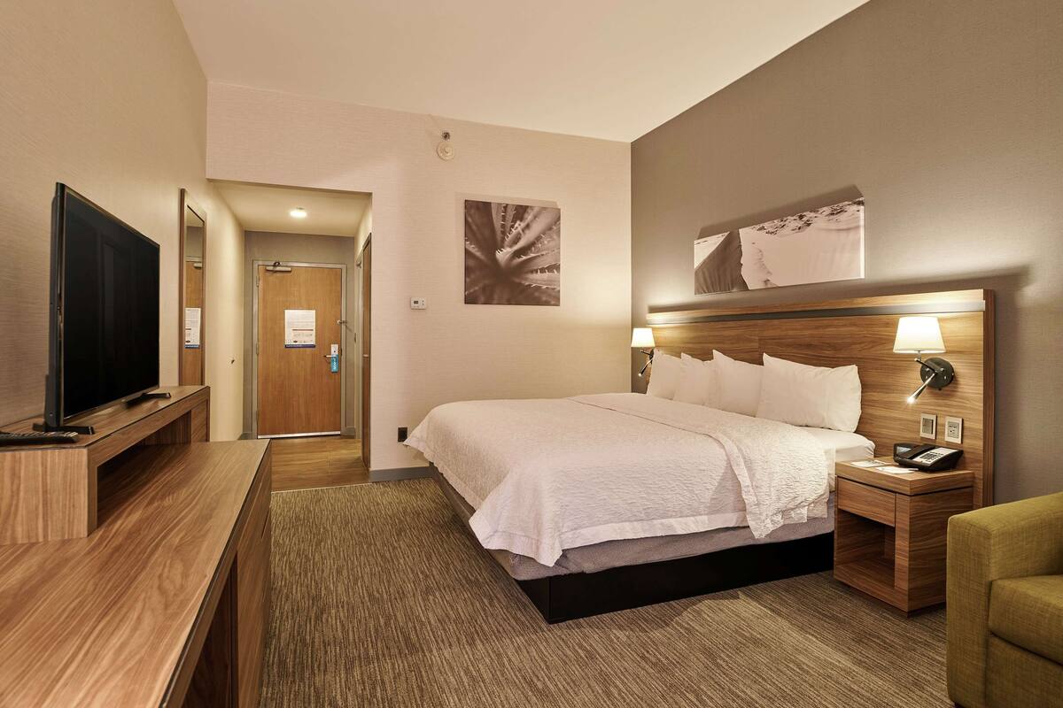 A hotel room with a bed, bedside table, lamp, and a TV on a stand.