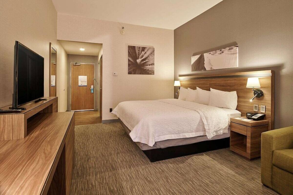 A hotel room with a bed, a TV, a bedside table, a lamp, and a chair.