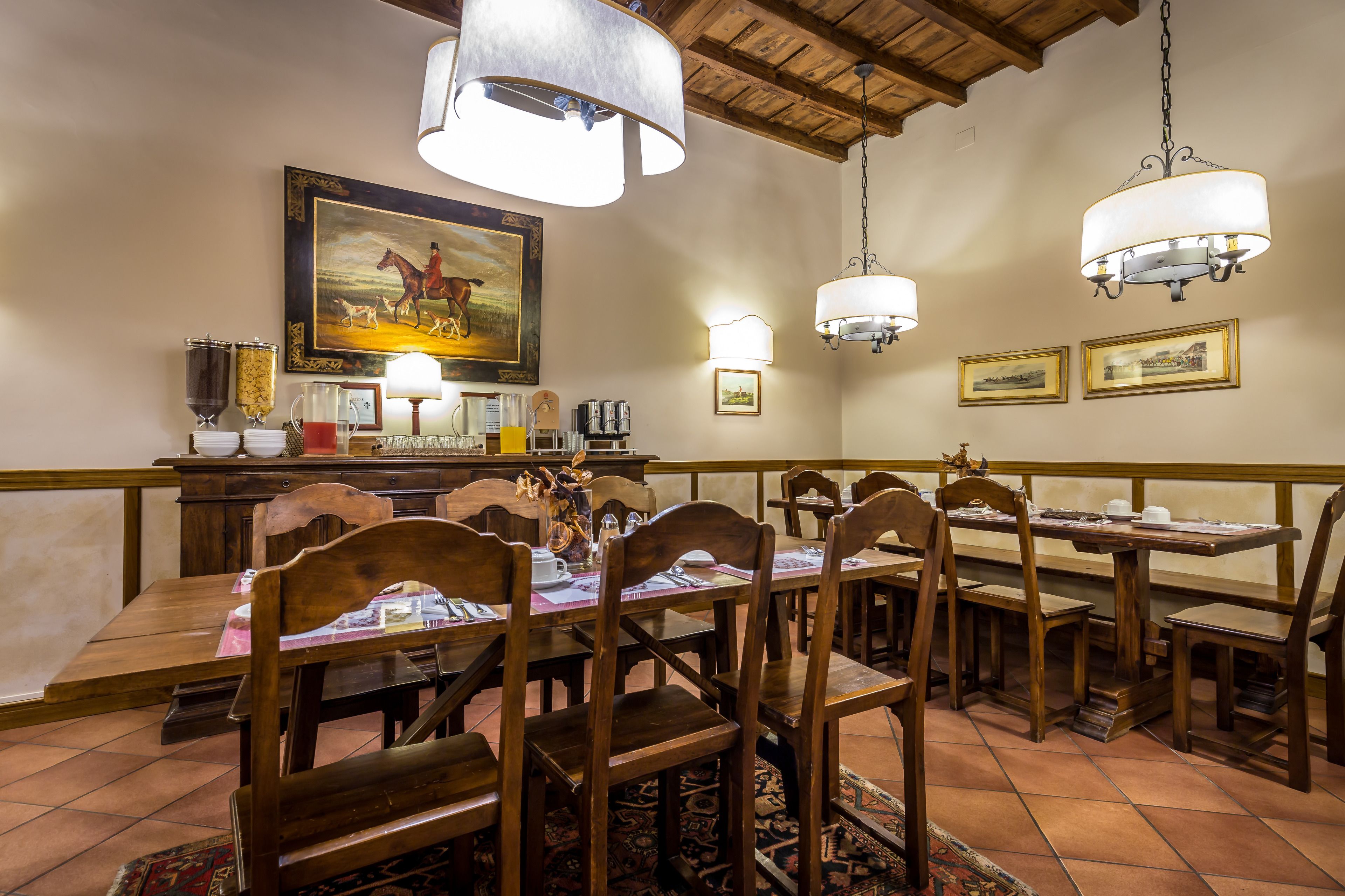 Un espace repas avec des tables et des chaises en bois, un tableau accroché au mur et des luminaires suspendus.