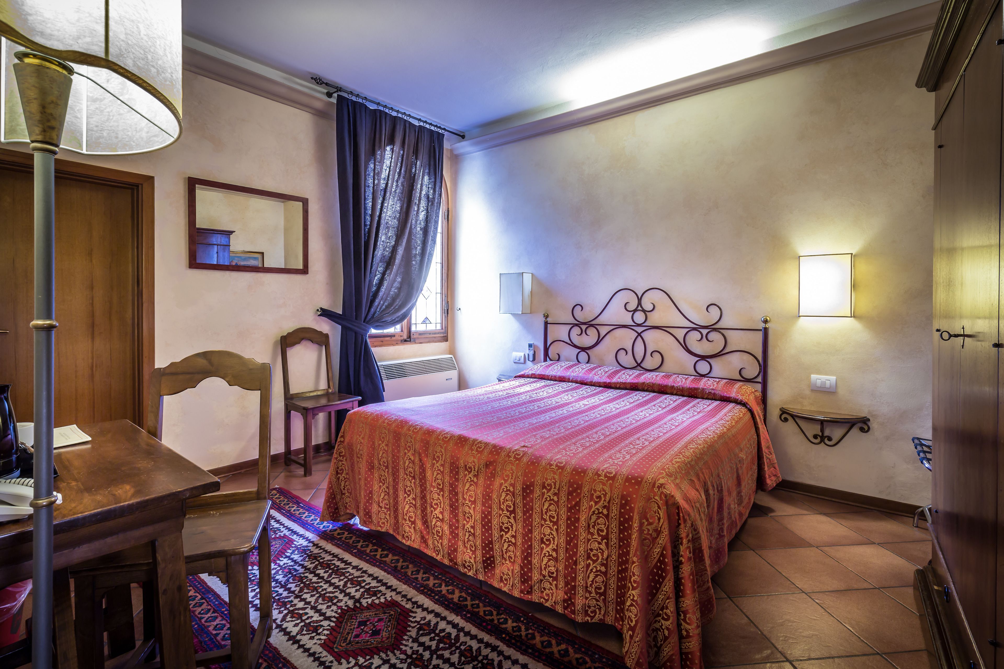 A bedroom with a bed, a desk, a chair, a lamp, and a nightstand.
