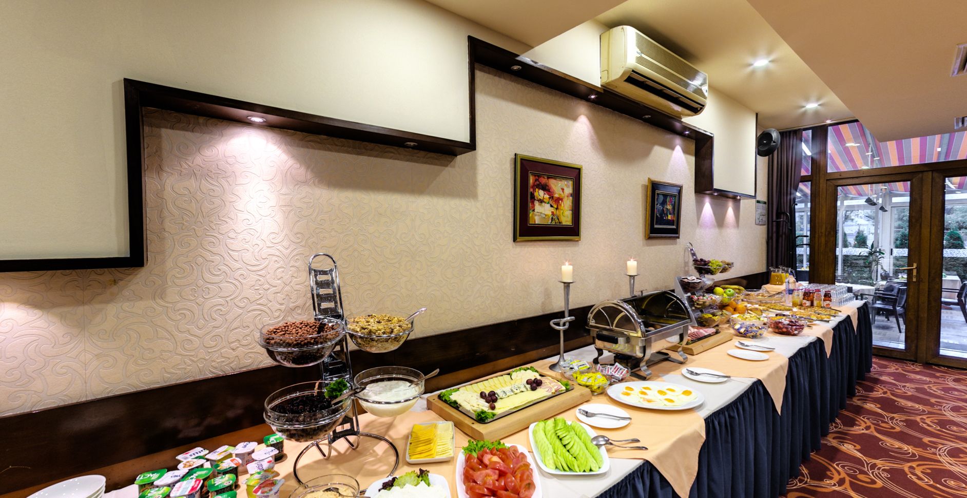 Un buffet proposant une variété de plats et un bar à salades, une bougie posée sur un chandelier et une grande fenêtre donnant sur un paysage verdoyant.