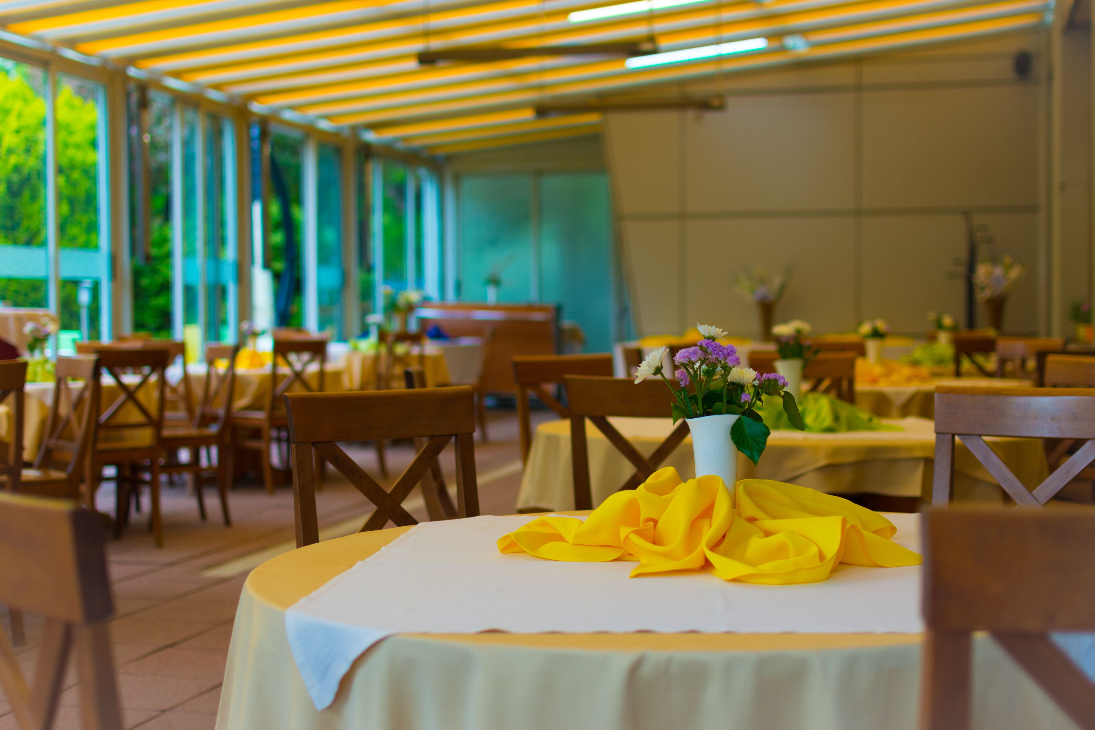 A covered outdoor dining area with tables set for a meal, featuring yellow tablecloths and a central floral arrangement.