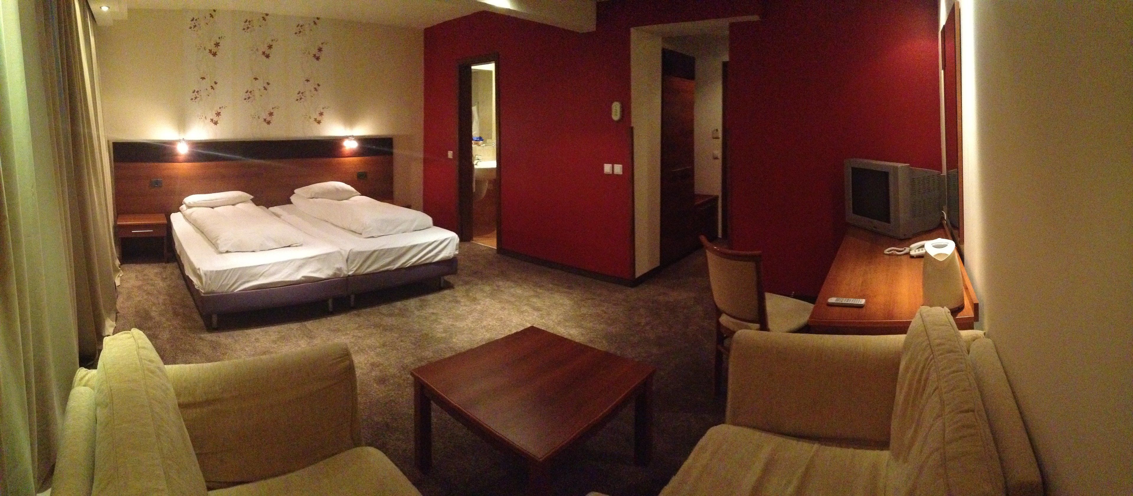 A hotel room with a bed, a desk, a chair, a TV, and a carpeted floor.