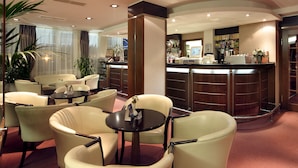 Un hall d’hôtel comprenant un bar, des espaces aménagés avec des sièges et un comptoir de réception.