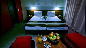 Une chambre d’hôtel avec un lit double, une table de chevet sur laquelle se trouve un panier de fruits, une tasse et un verre de jus d’orange.