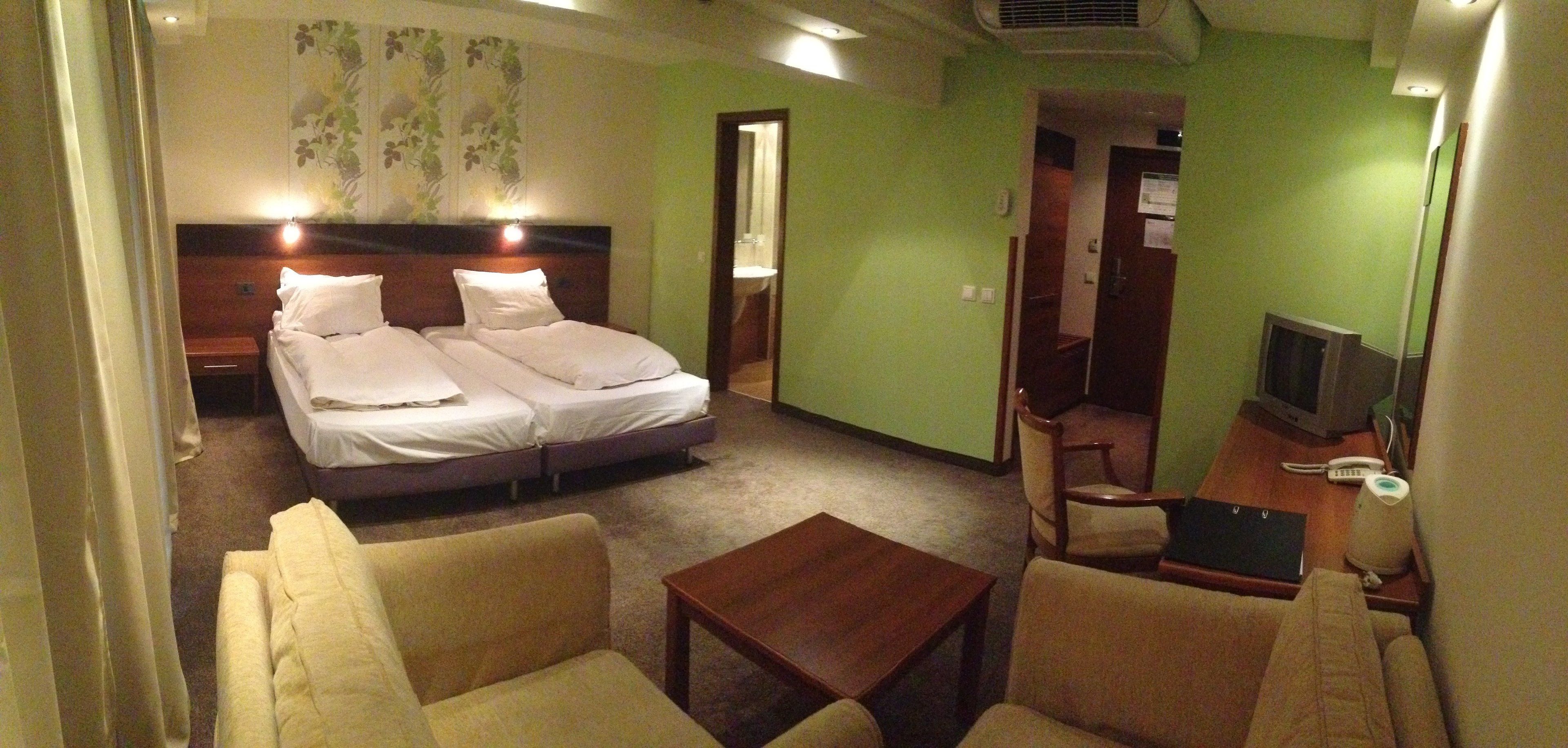 A hotel room with a bed, two bedside tables, a chair, a small table, and a television.