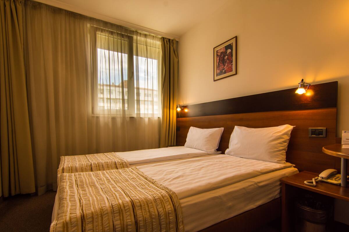 Habitación de hotel con dos camas, una mesita de noche con lámpara, teléfono y un cuadro en la pared.