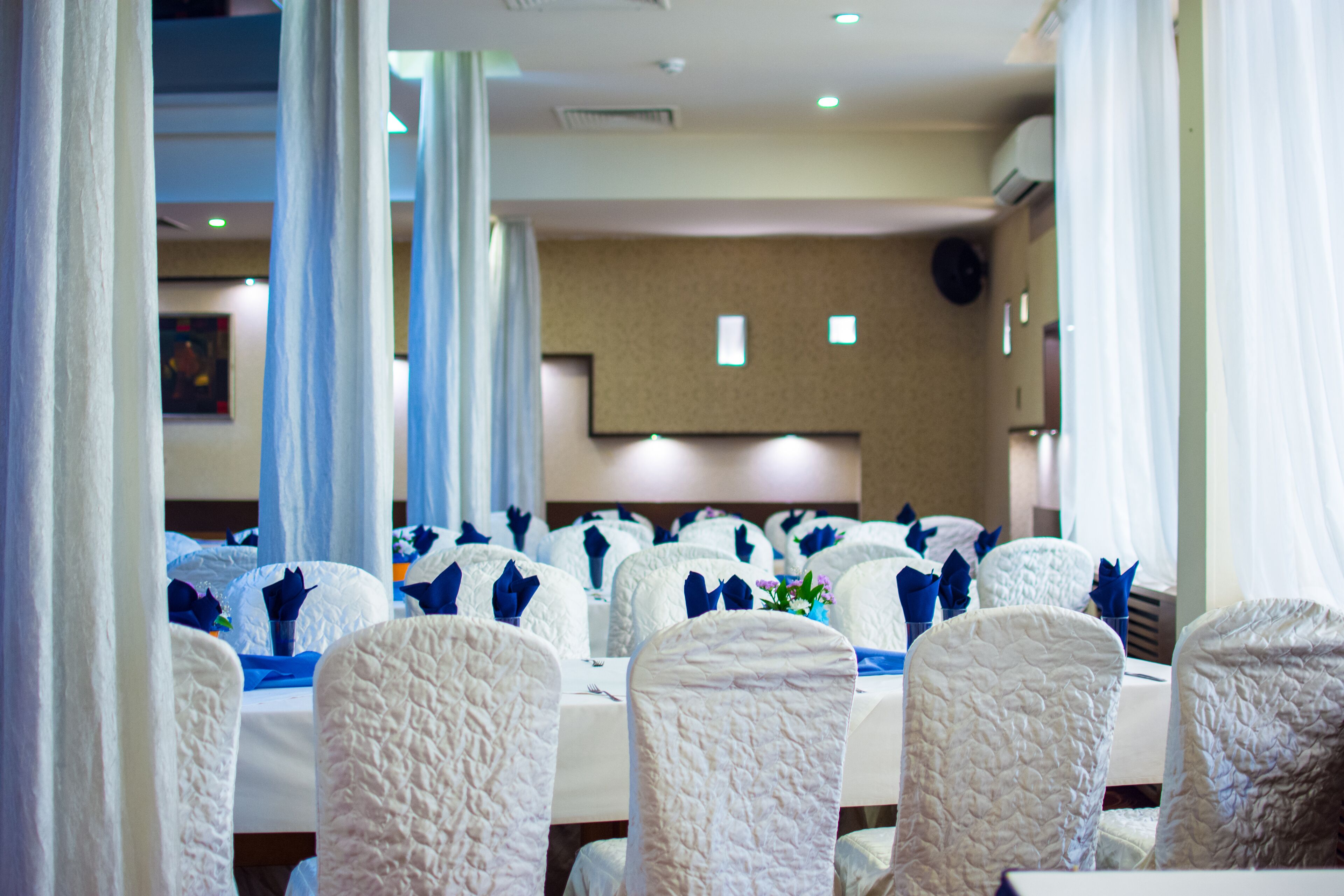 A banquet hall with rows of tables, each with white tablecloths and chairs covered in white fabric.