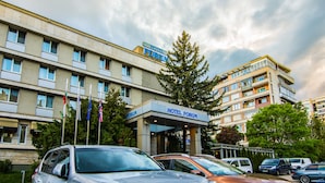 Un hôtel à étages, avec une entrée imposante et une enseigne bien visible, et plusieurs voitures garées devant.