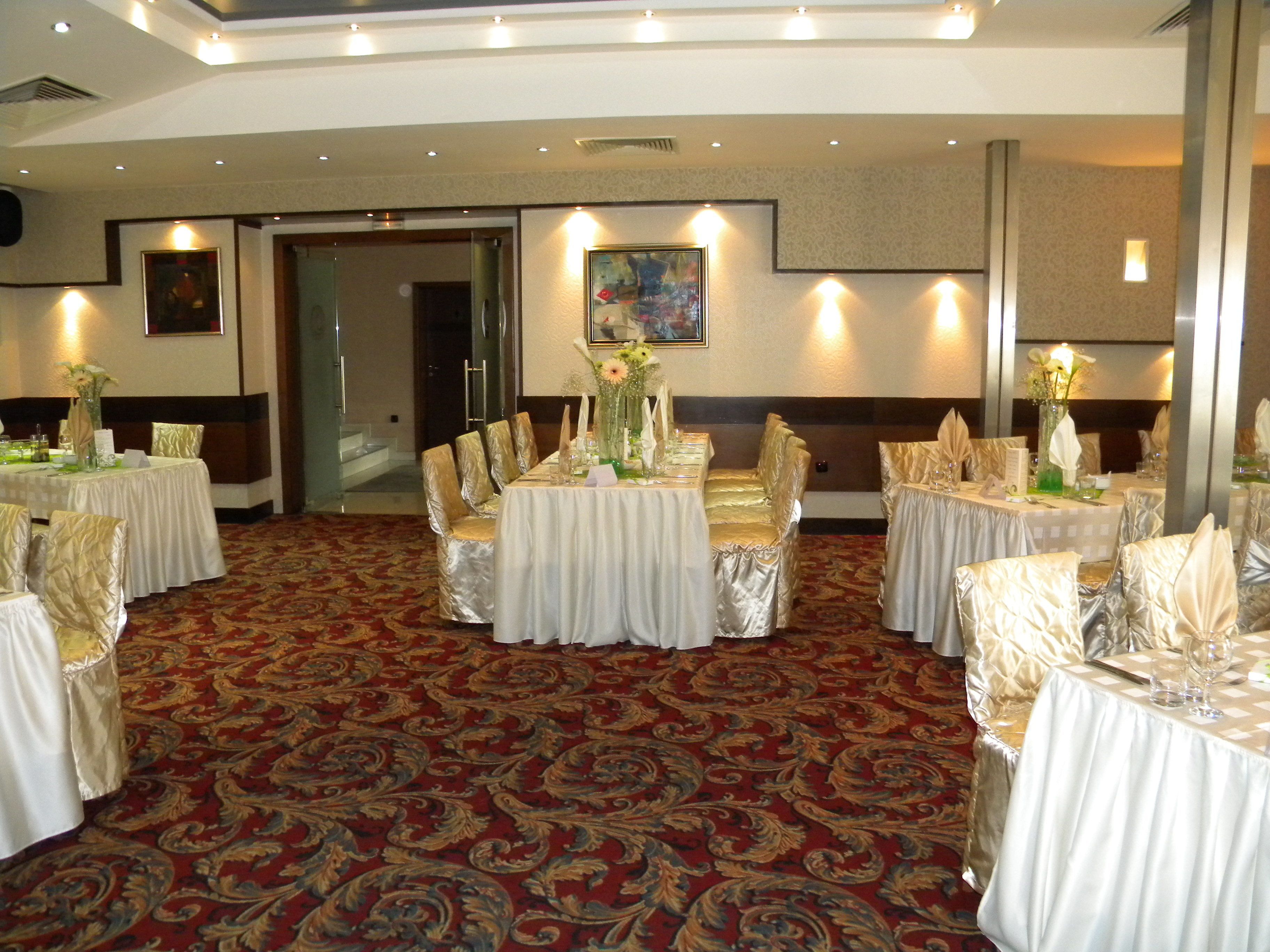 Une salle de banquet avec des tables rondes, des chaises recouvertes de housses et une moquette à motifs.