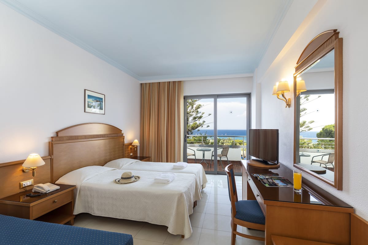 Habitación de hotel con dos camas, un escritorio con una computadora, un televisor y un balcón con vistas.