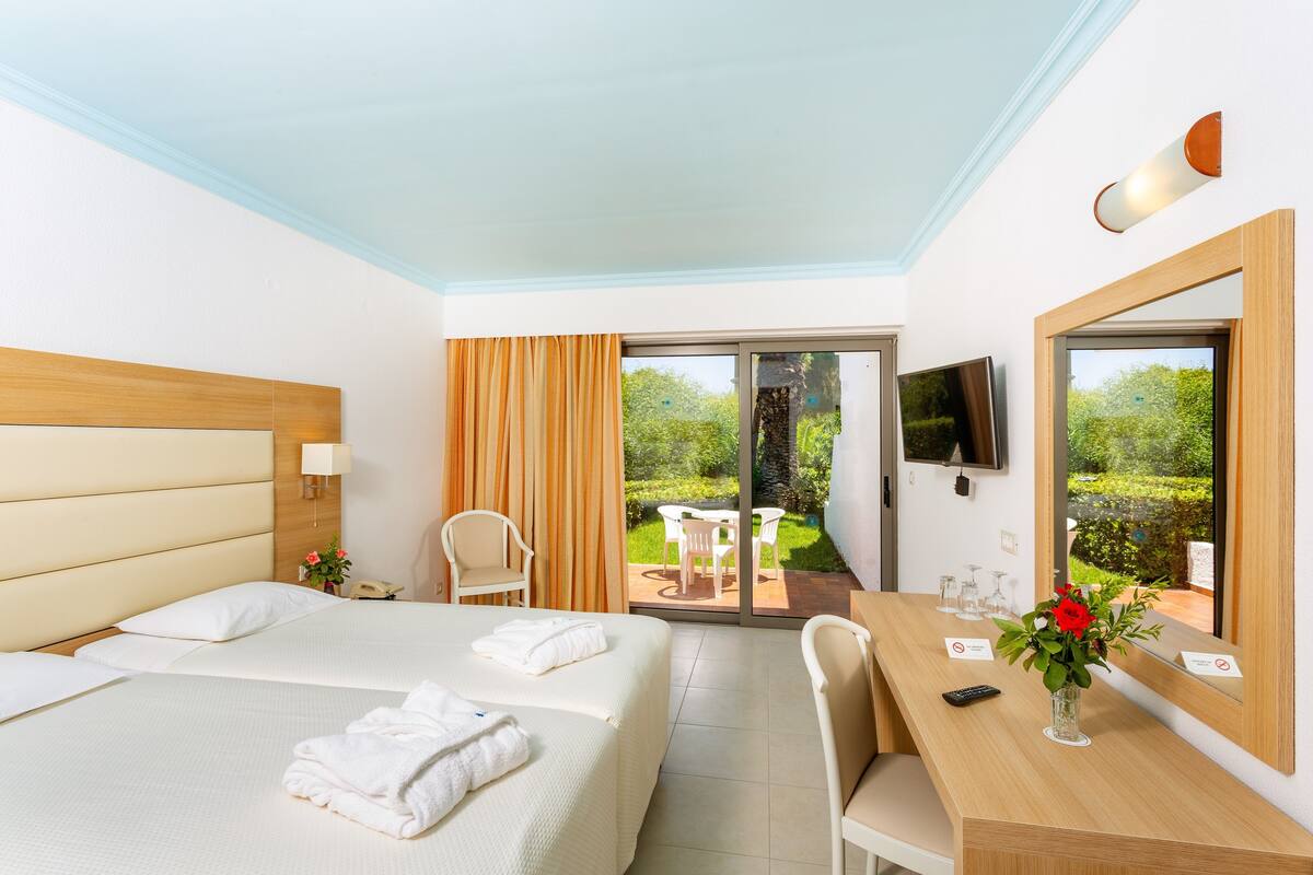 Habitación de hotel con cama, escritorio, silla, televisión y vista al jardín.