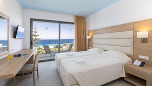 A hotel room with two beds, a desk with a chair, a TV, and a view of the ocean.