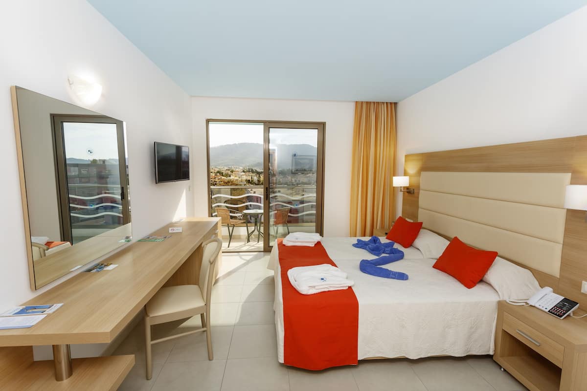 Una habitación de hotel con cama, mesita de noche, escritorio, silla y televisión.
