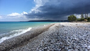A pebbled beach with a view of the sea and distant buildings.