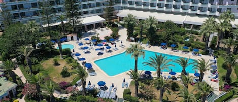 A hotel with a large pool surrounded by palm trees and sun loungers.