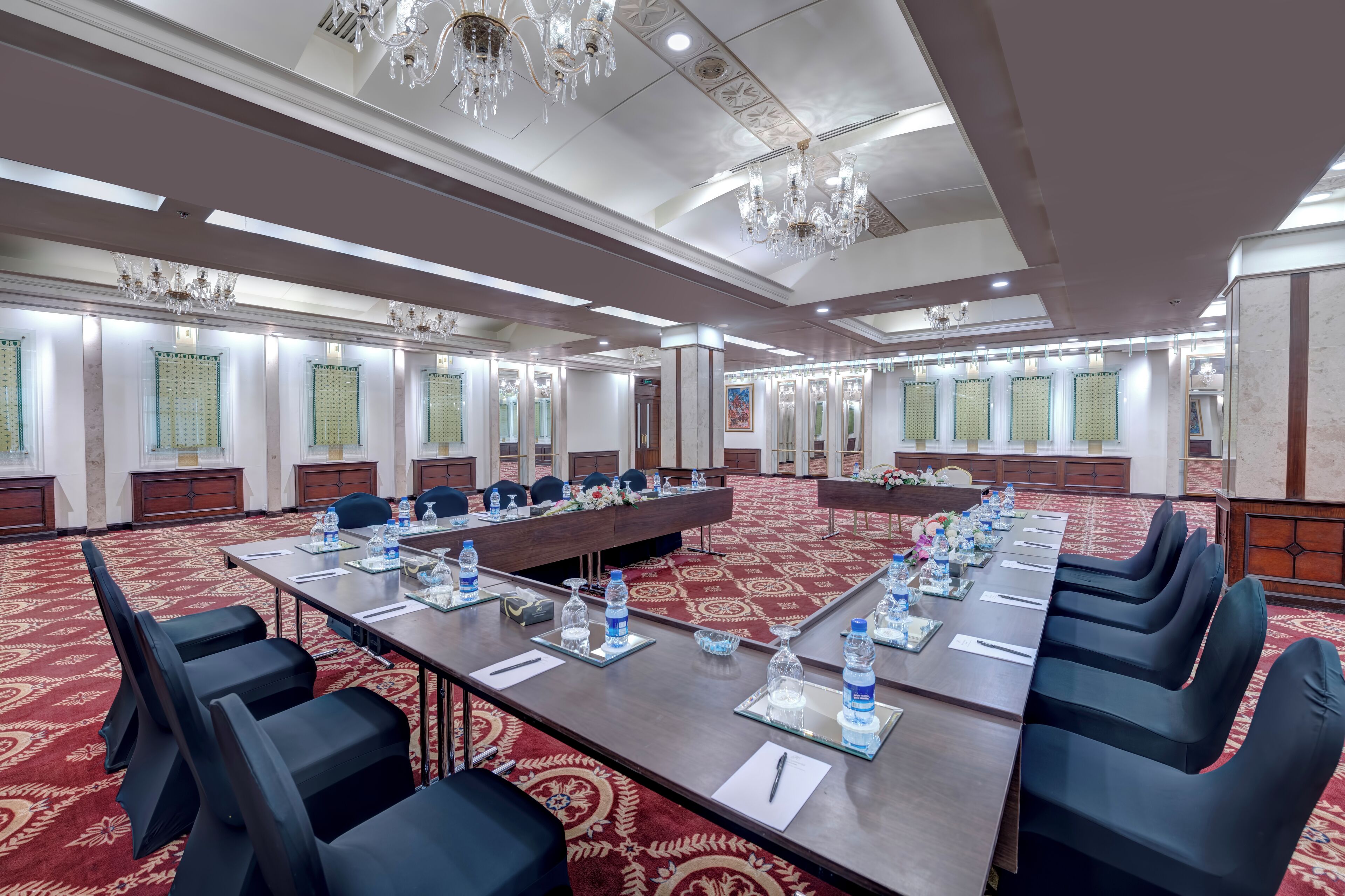 Un salón de conferencias amplio con una larga mesa, varias sillas y una alfombra roja.
