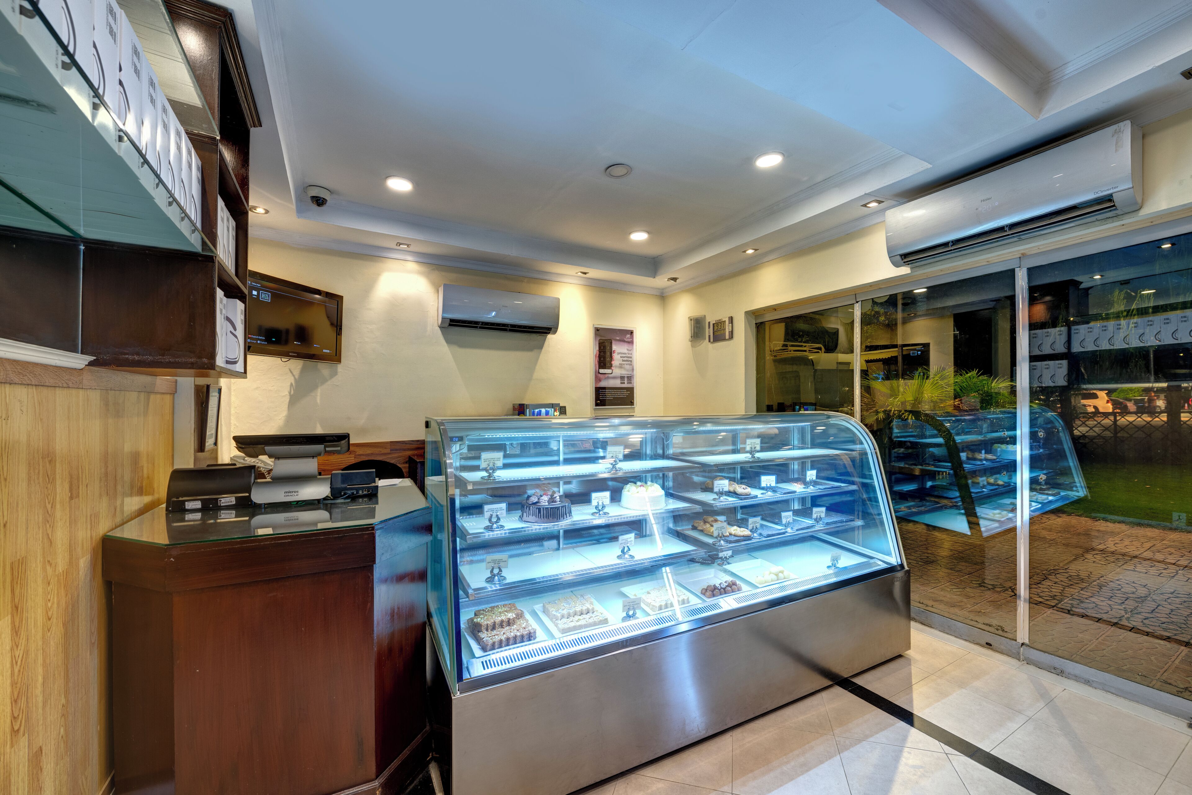 Vitrina de panadería con diversos productos horneados, un mostrador de recepción y una puerta de cristal que da al exterior.