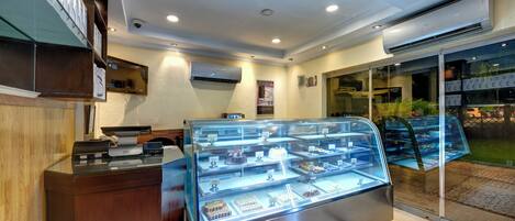 Vitrina de panadería con diversos productos horneados, un mostrador de recepción y una puerta de cristal que da al exterior.