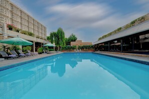 A swimming pool with lounge chairs and umbrellas, surrounded by buildings with balconies and greenery.