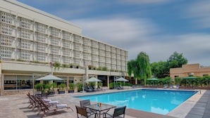 A swimming pool with lounge chairs and umbrellas, surrounded by a building with a patterned facade. - Pearl Continental Rawalpindi (Rawalpindi)