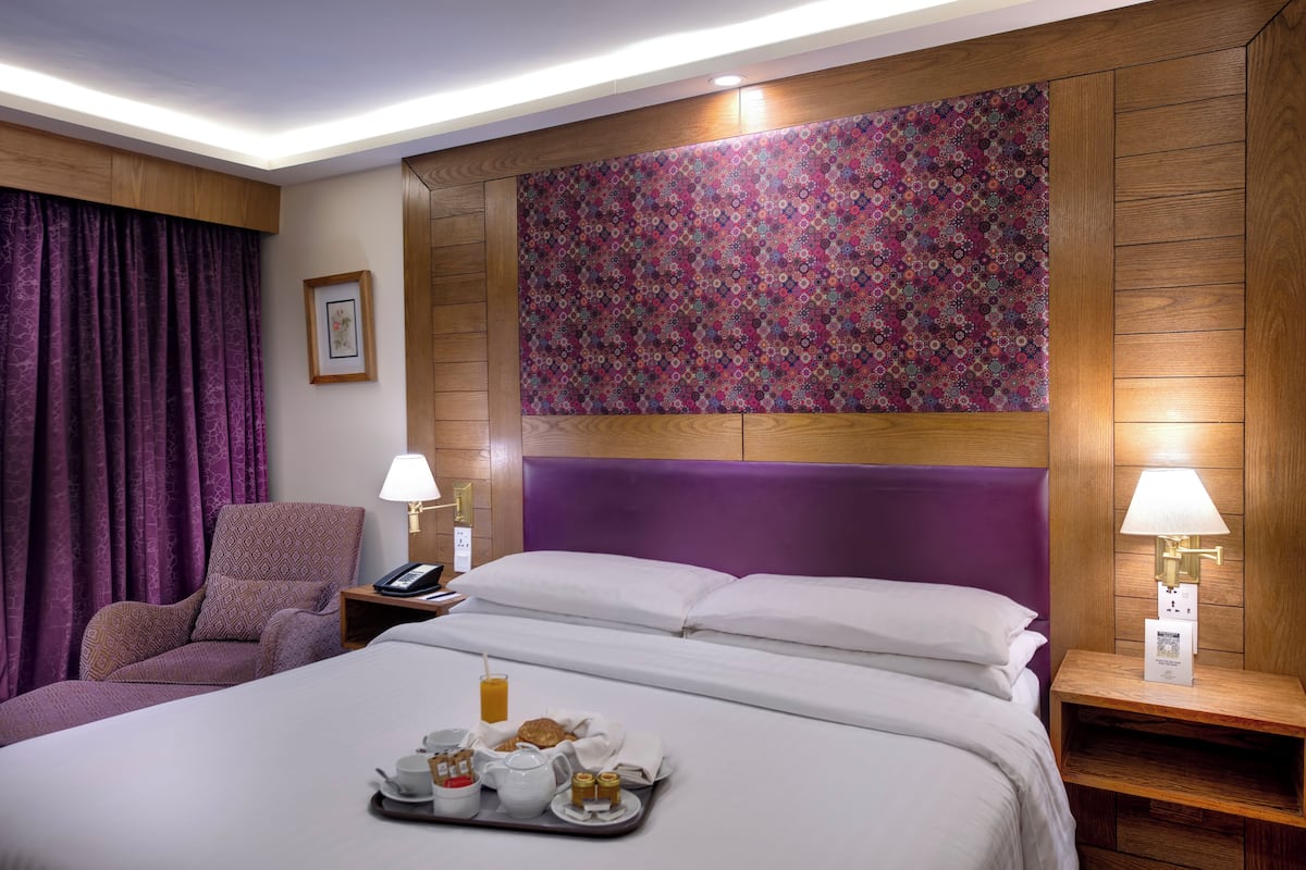 Une chambre d’hôtel avec un grand lit, une chaise, une table de chevet avec une lampe et un plateau contenant des articles pour le petit-déjeuner.