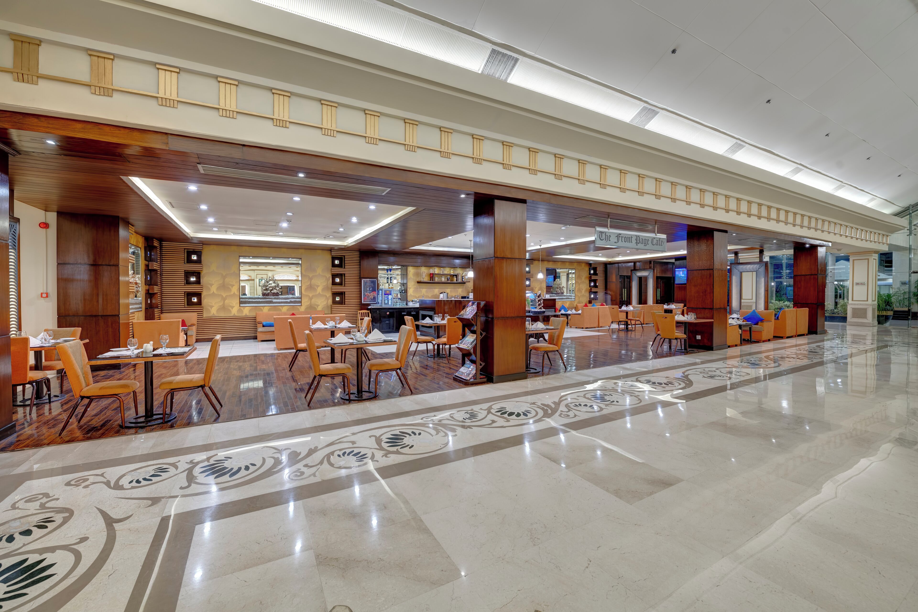 A spacious hotel lobby with a long reception desk, multiple seating areas, and a polished marble floor.