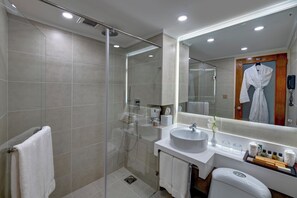A modern bathroom with a glass-enclosed shower, a large mirror, a white sink, and a robe hanging on a wooden door.