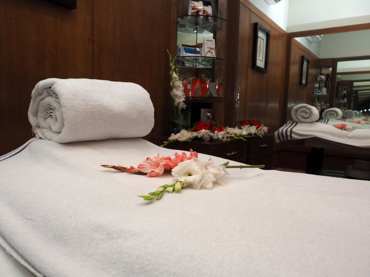 Una cama bien hecha con una toalla blanca enrollada y un arreglo floral sobre la cama.