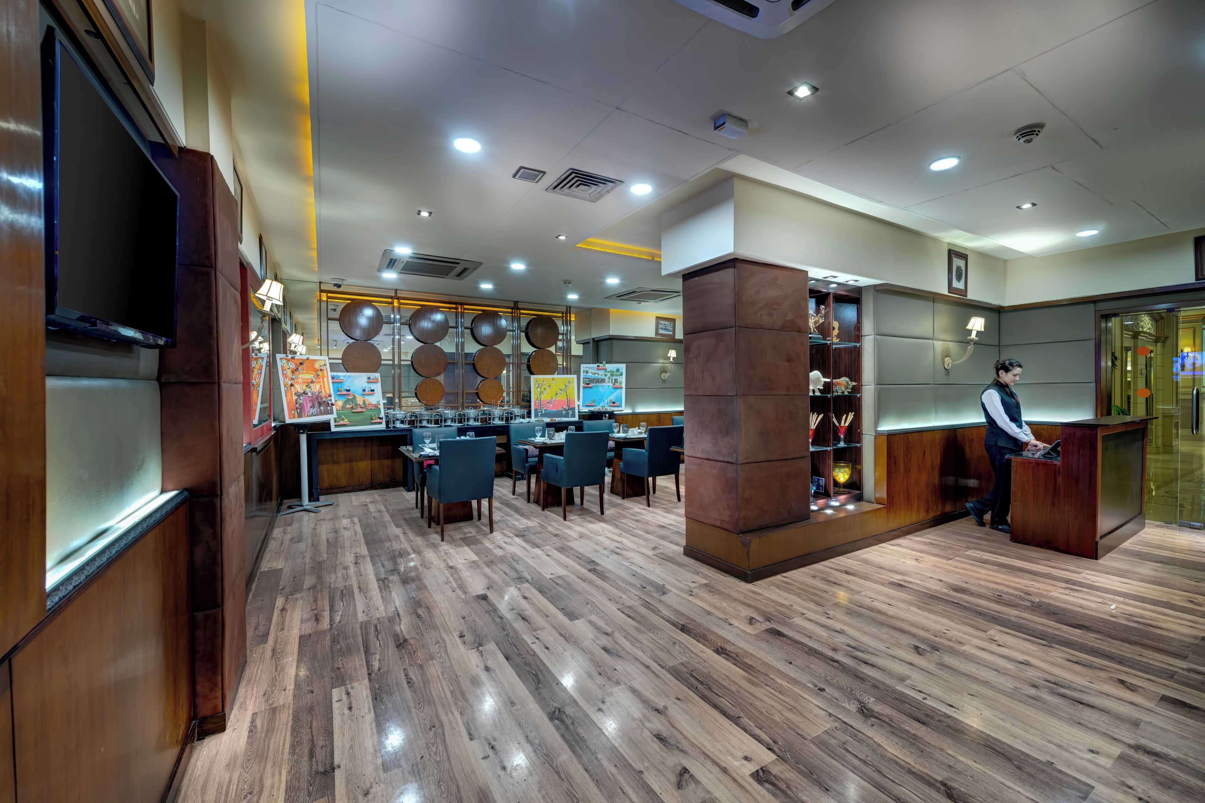 Un restaurante amplio con suelo de madera, varias mesas y una zona de recepción con mostrador y una persona detrás.