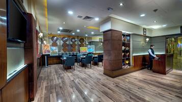 Un restaurante amplio con suelo de madera, varias mesas y una zona de recepción con mostrador y una persona detrás.