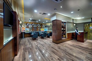 Un restaurante amplio con suelo de madera, varias mesas y una zona de recepción con mostrador y una persona detrás.