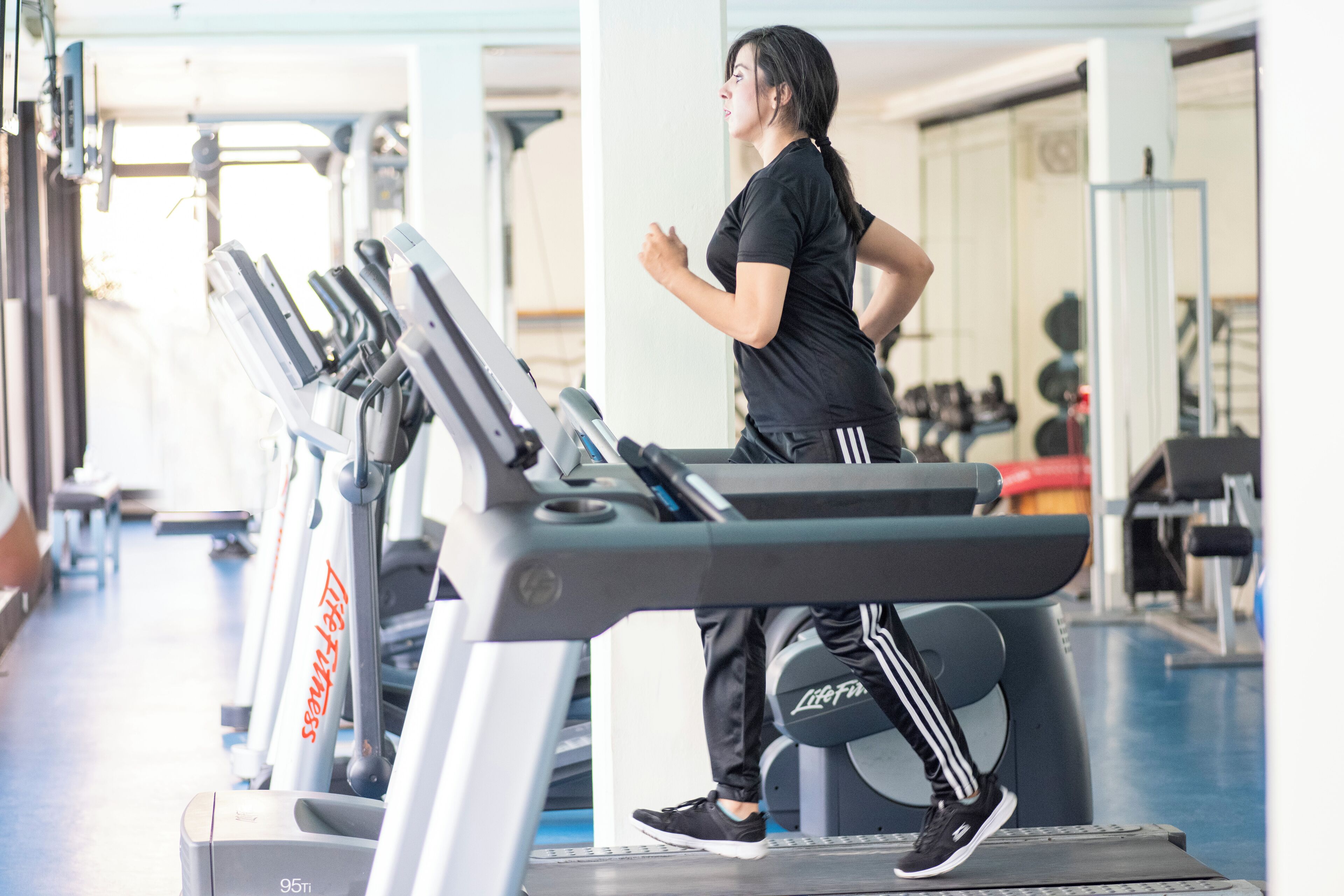 A person running on a treadmill in a gym with exercise equipment in the background.