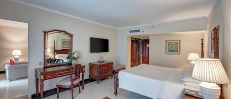 A hotel room with a bed, a desk with a chair, a television, a dresser, and a dining table with fruit.
