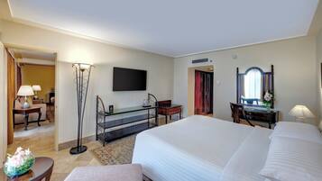 Habitación de hotel con una cama grande, un televisor de pantalla plana montado en la pared, un escritorio con lámpara, un espejo y vista al pasillo.
