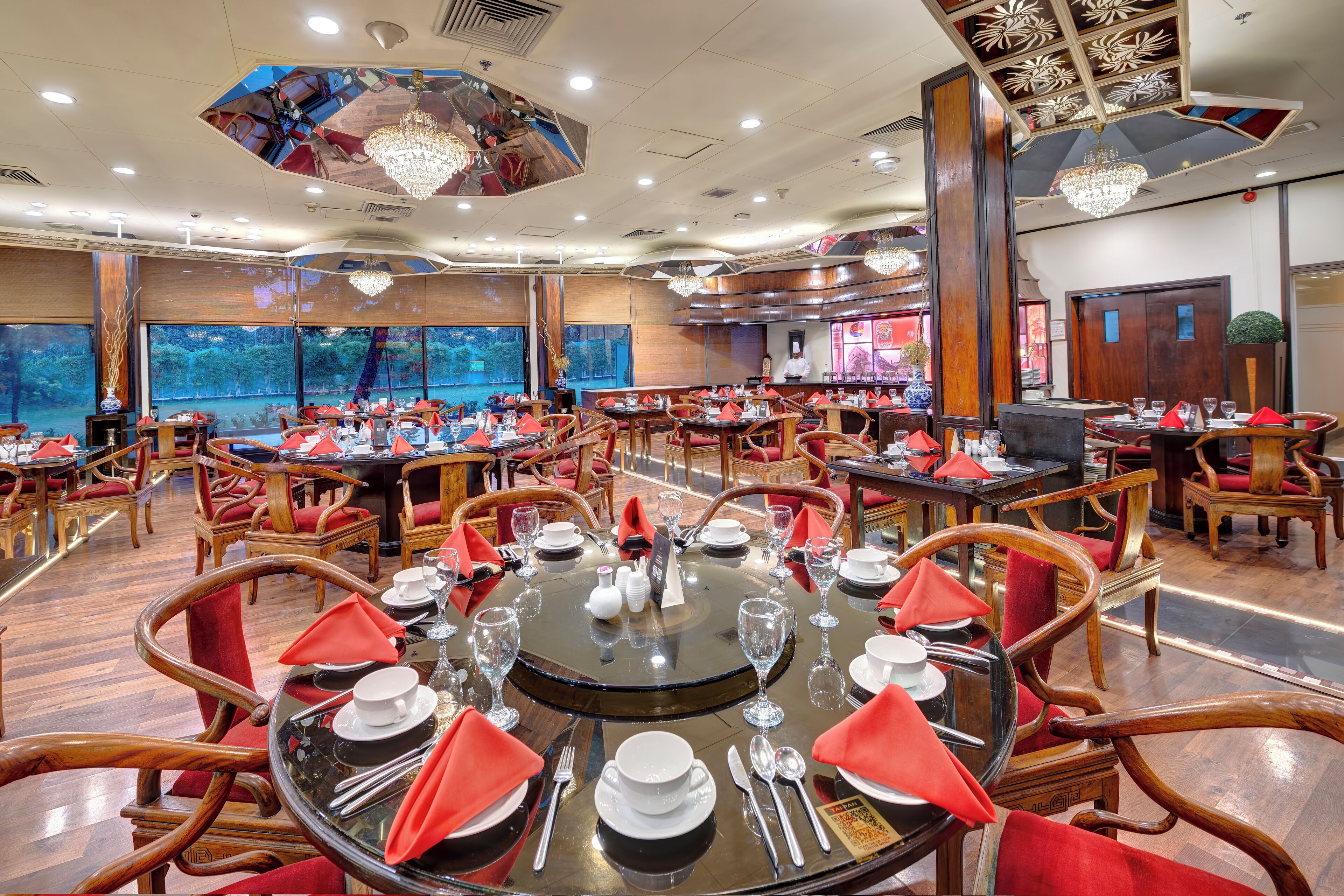 Un restaurante con mesas redondas dispuestas para comer, sillas de madera y servilletas rojas.