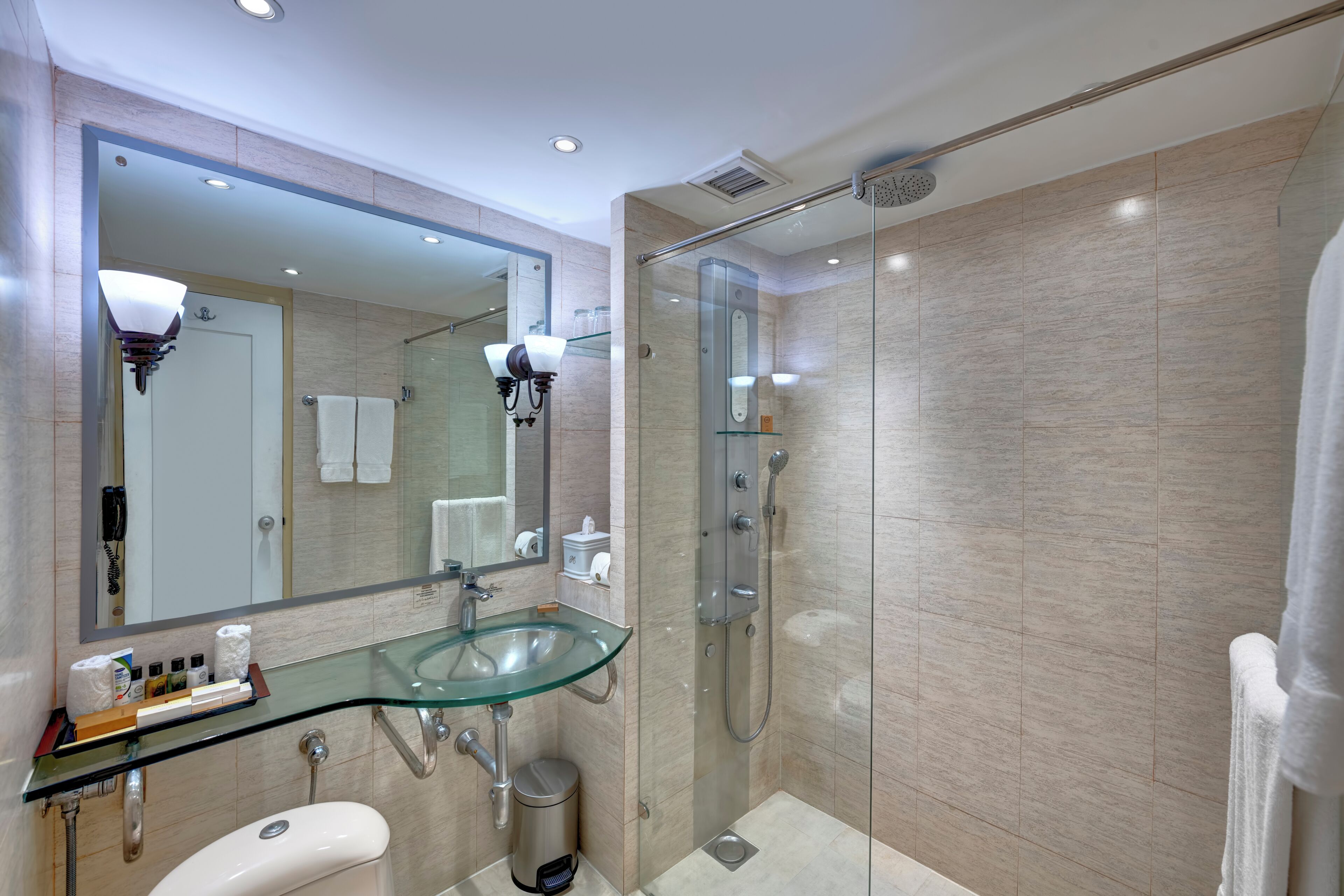 Un baño moderno con un lavabo de vidrio, ducha a ras de suelo y un espejo grande.