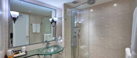 Un baño moderno con un lavabo de vidrio, ducha a ras de suelo y un espejo grande.