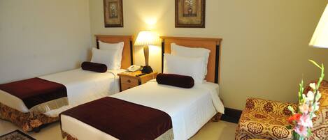 A hotel room with two beds, a nightstand, a lamp, a chair, and a small table with a vase of flowers.