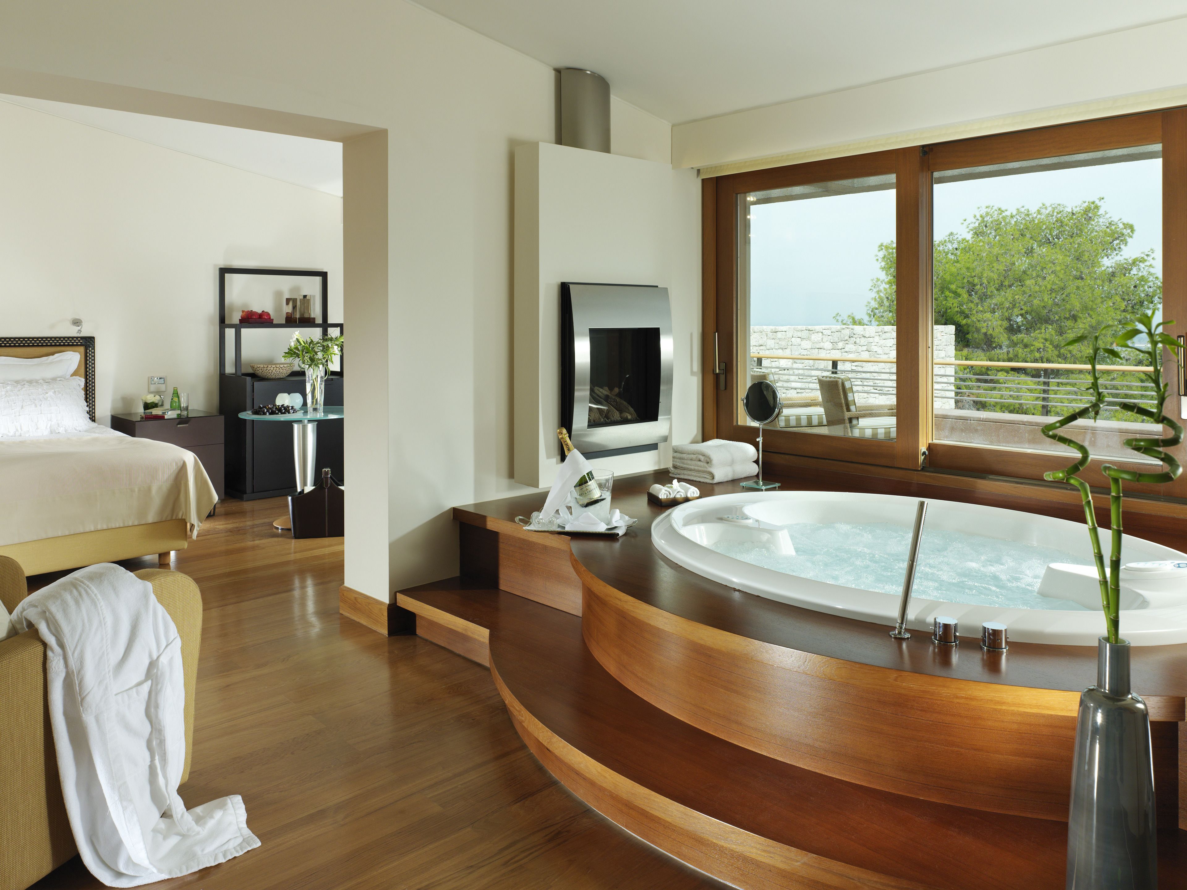 A modern hotel room with a large bed, a sitting area with a view, a jacuzzi, and a balcony with a view.