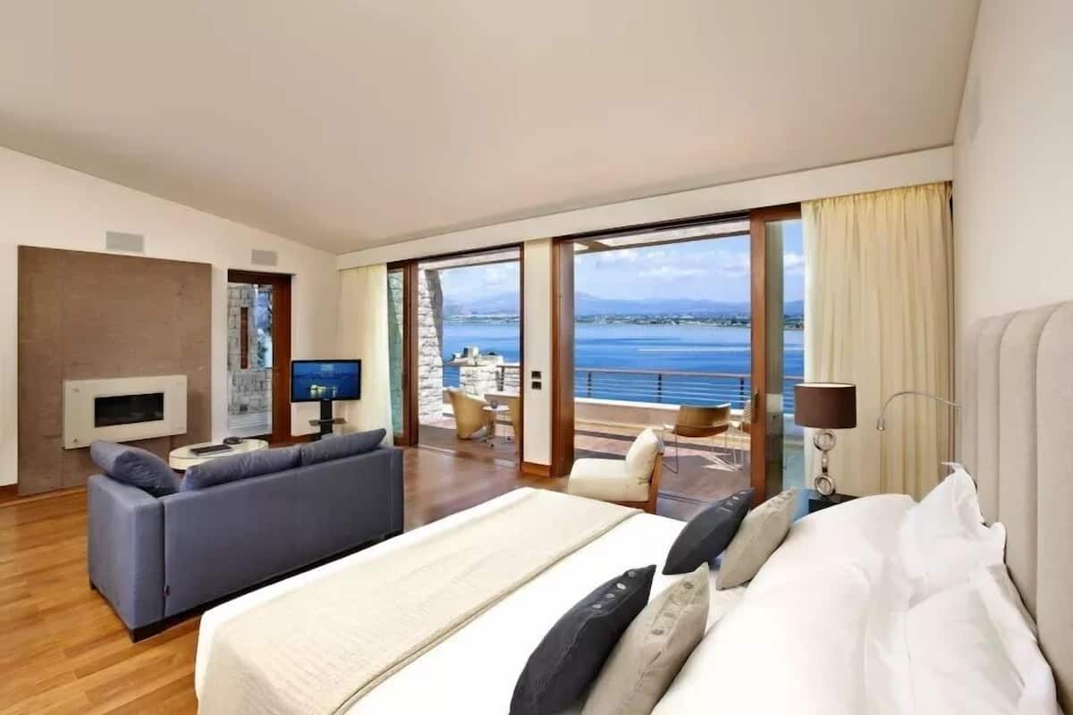 Ein Hotelzimmer mit einem großen Bett, einer Sitzecke, einem Fernseher und einem Balkon mit Meerblick.