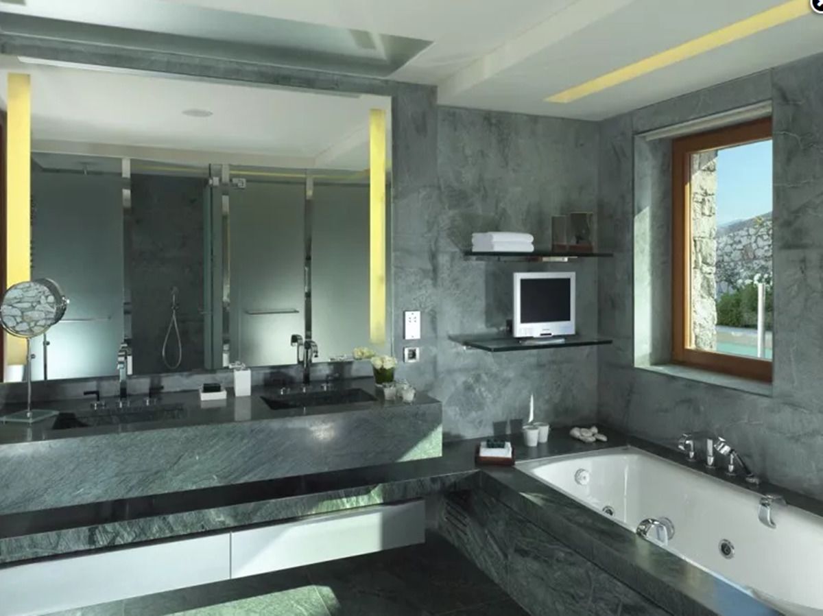 A modern bathroom with a large vanity, a bathtub, and a small shelf with a television.