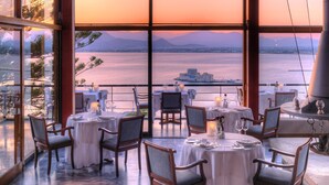 Een restaurant met gedekte tafels, met uitzicht op een waterpartij en bergen.
