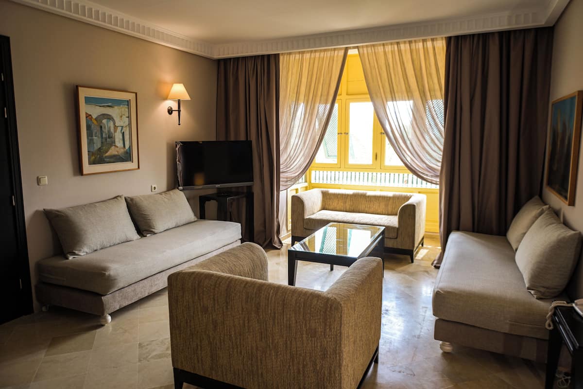 Un salon comprenant un canapé, des fauteuils, une table basse, un téléviseur et une fenêtre avec des rideaux.