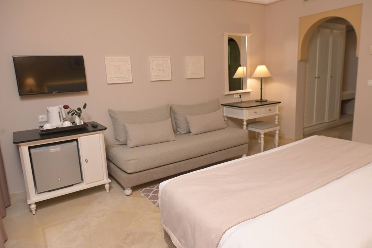 Une chambre d’hôtel comprenant un lit, un canapé, une télévision, un bureau avec une lampe et une armoire.