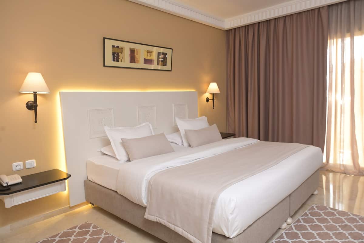 Une chambre d’hôtel avec un grand lit, des lampes de chevet, une table de nuit et un tableau encadré au mur.