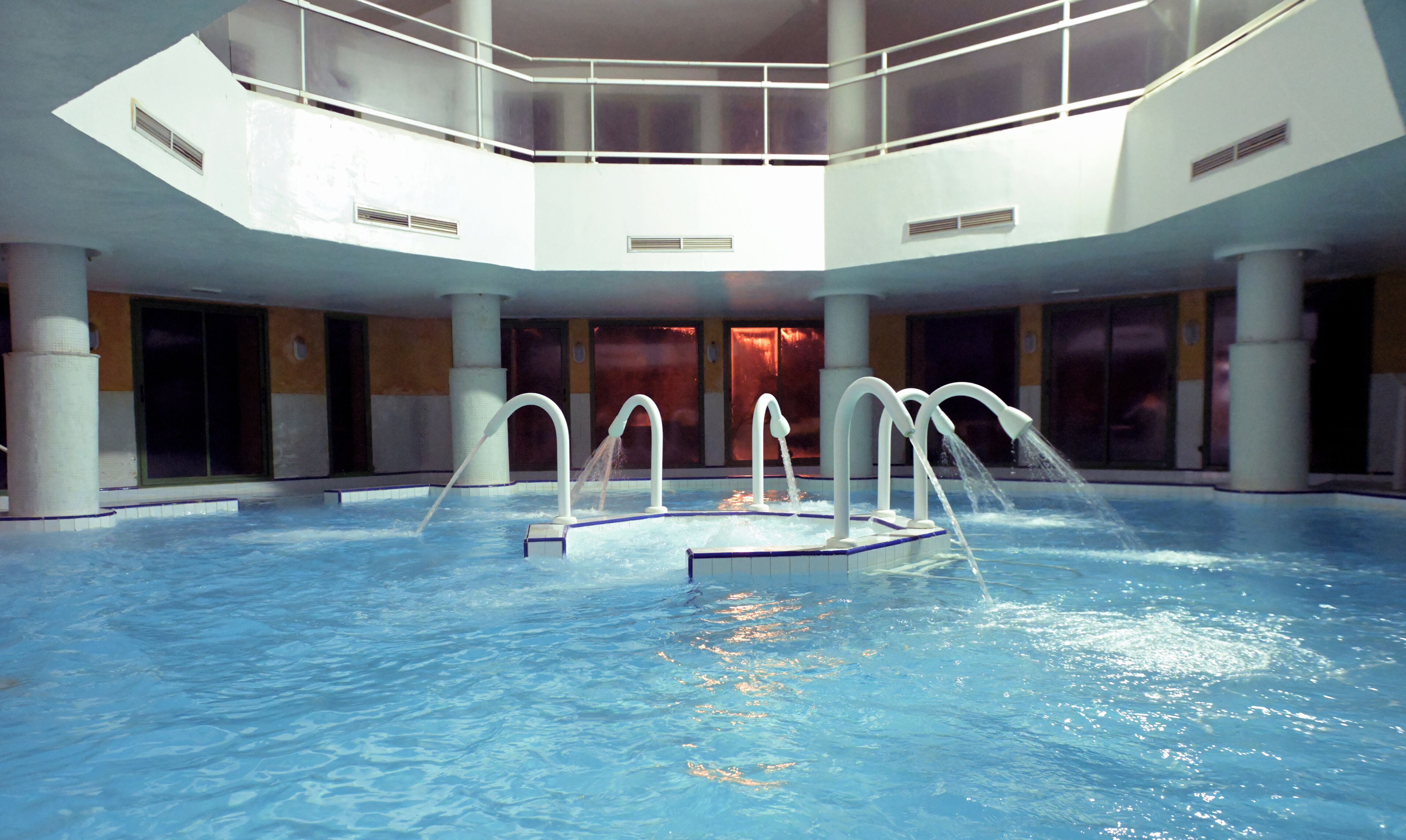 Ein Innenpool mit mehreren Wasserstrahlen, einer hohen Decke und großen Fenstern.
