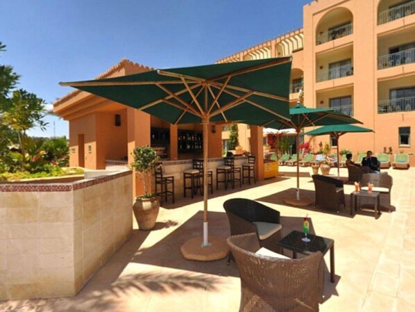 An outdoor patio area with wicker furniture, green umbrellas, and a bar. - Hotel Alhambra Thalasso (Hammamet)