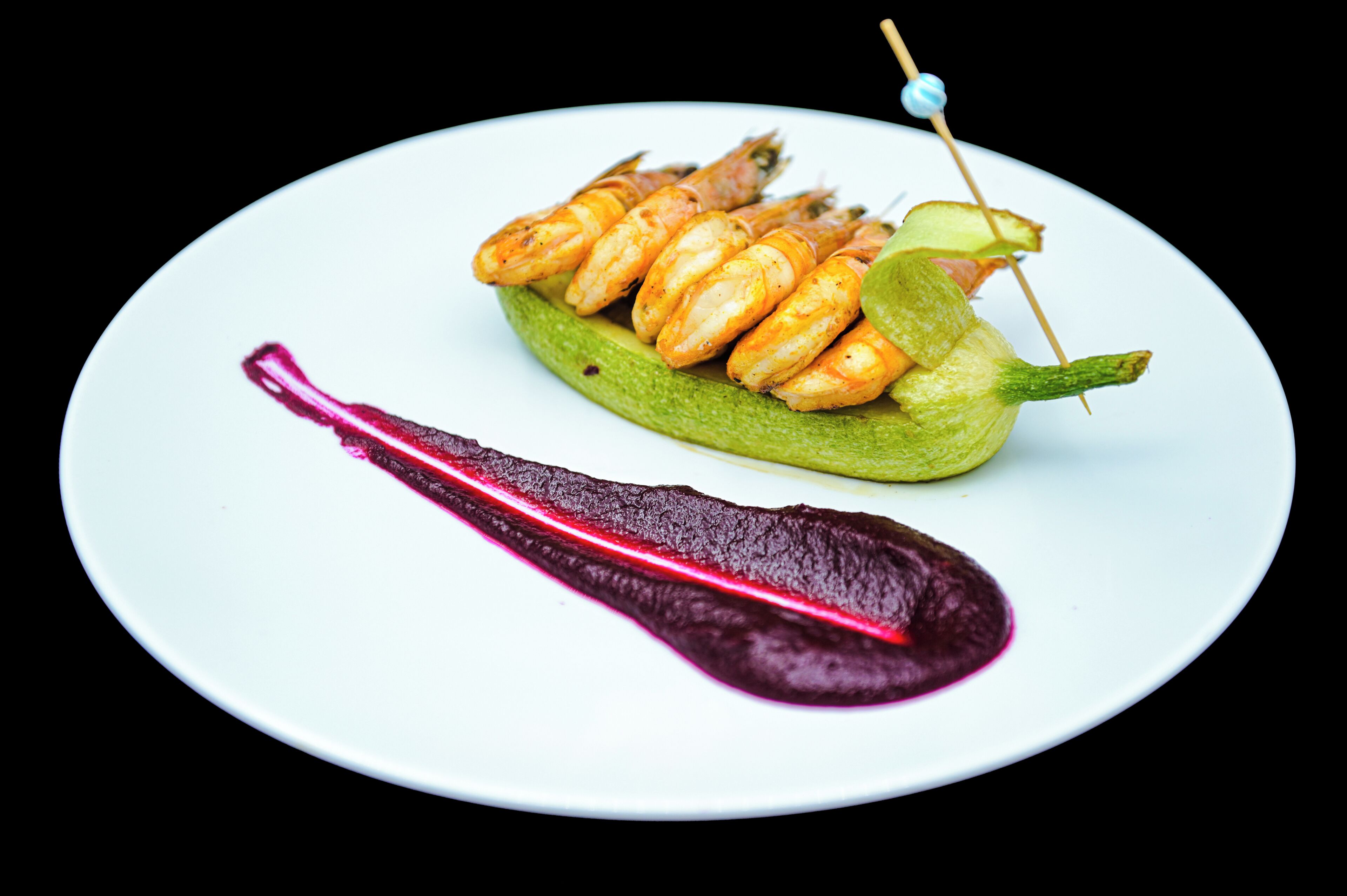 Um prato com camarões grelhados, um vegetal verde e um molho roxo.